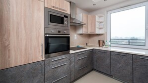 A modern kitchen with wooden cabinets, stainless steel appliances, and a large window providing a view. - Częstochowska Urban Comfort Apartment (Łódź)