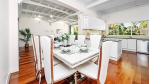 A dining area with a marble table, white chairs, and a view of the kitchen. - Stathfield Stylish 6br house with Pool/Tennis (Strathfield)