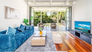 A modern living room with a blue sofa, a coffee table, and a TV on a wooden stand. - Stathfield Stylish 6br house with Pool/Tennis (Strathfield)