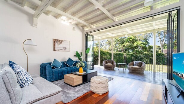 A modern living room with a sofa, armchair, and a coffee table. There is a TV on the right side and a large window providing a view of the outdoors. - Stathfield Stylish 6br house with Pool/Tennis (Strathfield)