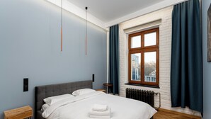 A modern bedroom with a large bed, a nightstand, a radiator, and a window with curtains. - Świętej Gertrudy Chic Apartment (Kraków)