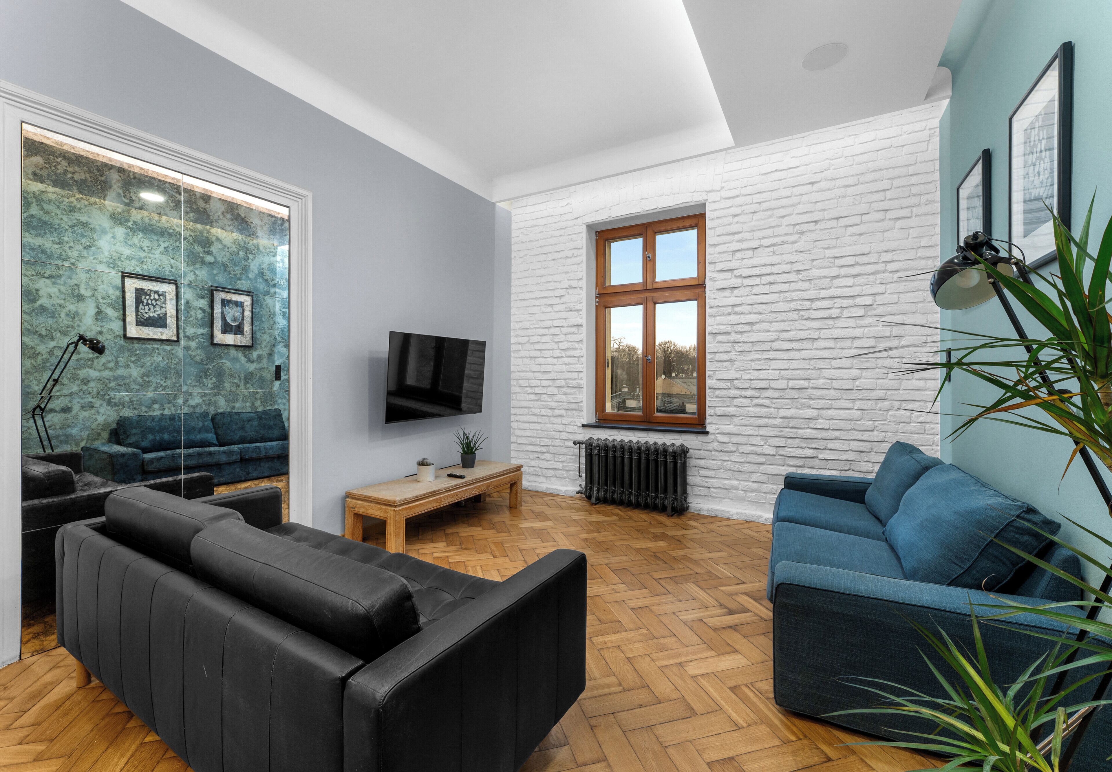 Una sala de estar moderna con un sofá de cuero negro, un sofá azul, una mesa de centro de madera y un televisor.