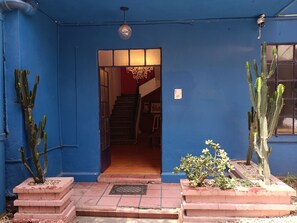 Une entrée bleue, avec un escalier menant à l’intérieur, entourée de cactus en pot.
