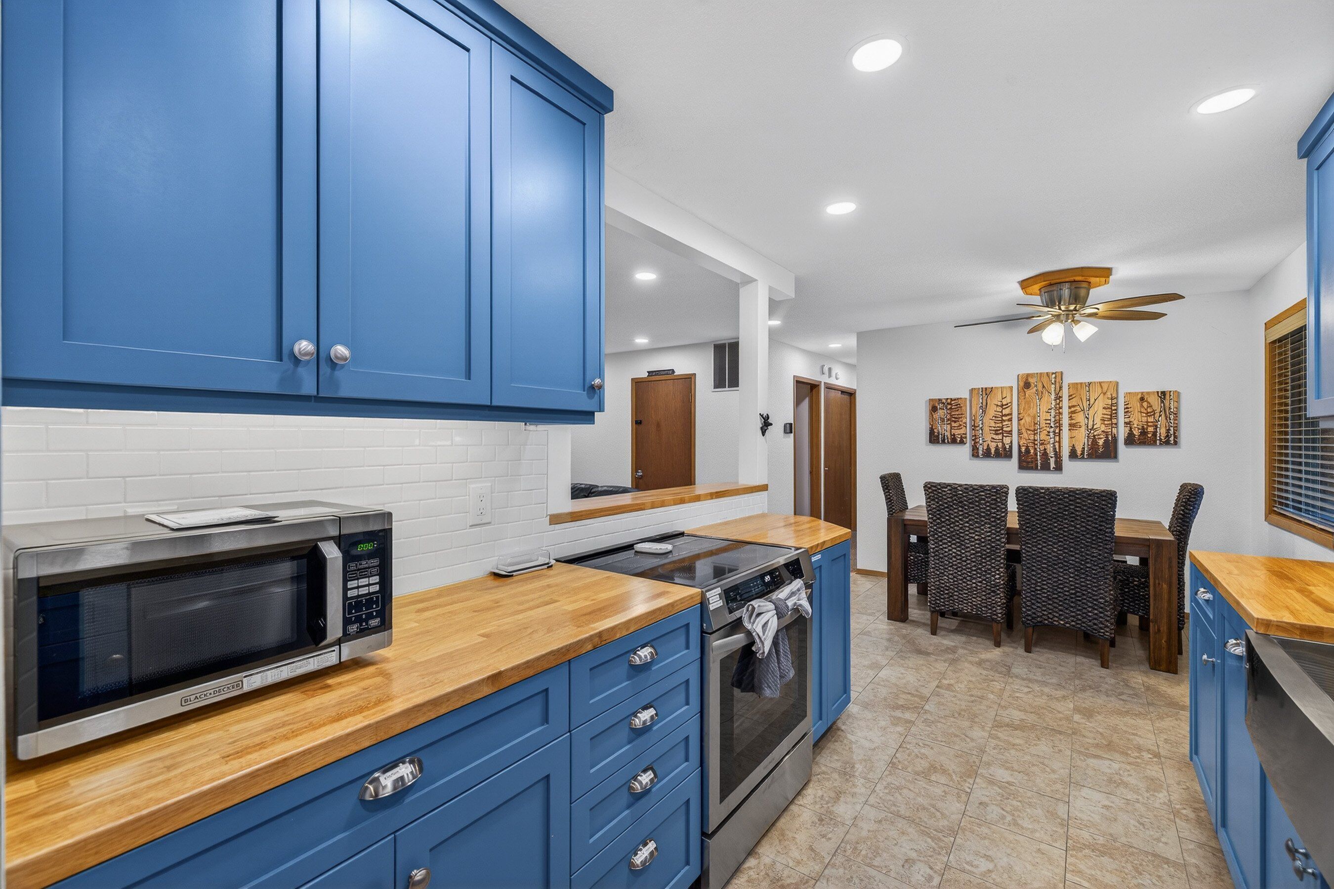 A kitchen with blue cabinets, a microwave, stove, and a dining area with a table and chairs.