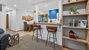 A modern kitchen with a bar area, wooden shelves, and a dining set. - Evergreen Escape- Great location near downtown w/trailer parking and fully fenced yard (McCall)