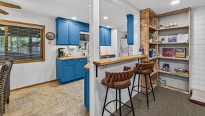 A kitchen with blue cabinets, a wooden bar counter, and two bar stools. - Evergreen Escape- Great location near downtown w/trailer parking and fully fenced yard (McCall)