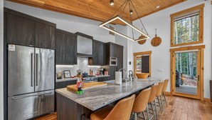 Una cocina moderna con armarios oscuros, electrodomésticos de acero inoxidable, encimera de granito y techo de madera.