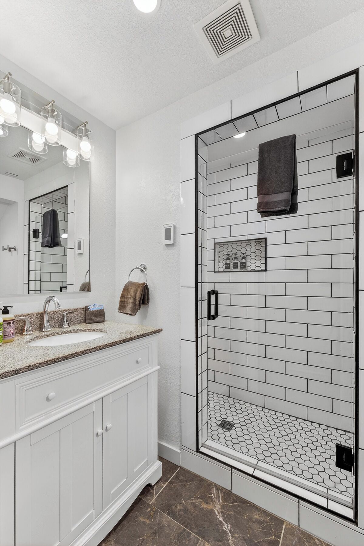 Une salle de bain moderne avec des meubles blancs, un grand miroir, une douche en verre et un pare-splash en carrelage.
