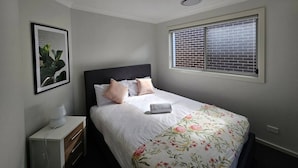 A bedroom with a bed, a nightstand, a framed picture, and a window with blinds.