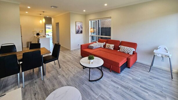 A modern living room with a red sofa, a dining table with chairs, and a white high chair.