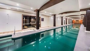 Una piscina interior amplia con agua cristalina, rodeada por un diseño arquitectónico moderno con vigas de madera y suelo de baldosas.