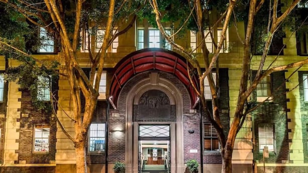 Un edificio con una entrada arqueada destacada, una escalera que conduce a la entrada y árboles enmarcando la escena.
