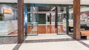 Entrada de hotel con puerta de cristal, pilares de madera, mostrador de recepción y un mostrador de check-in.