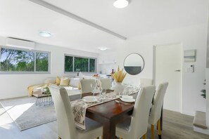 A modern dining area with a wooden table set for four, surrounded by white chairs. - Collaroy 3Br with pool / Breath and Relax (Collaroy)