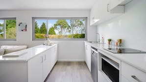 A modern kitchen with white cabinetry, a built-in oven, and a window overlooking greenery. - Collaroy 3Br with pool / Breath and Relax (Collaroy)