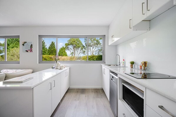 A modern kitchen with white cabinetry, a built-in oven, and a window overlooking greenery. - Collaroy 3Br with pool / Breath and Relax (Collaroy)