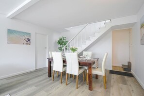 A dining area with a wooden table and white chairs, a staircase, and a painting on the wall. - Collaroy 3Br with pool / Breath and Relax (Collaroy)