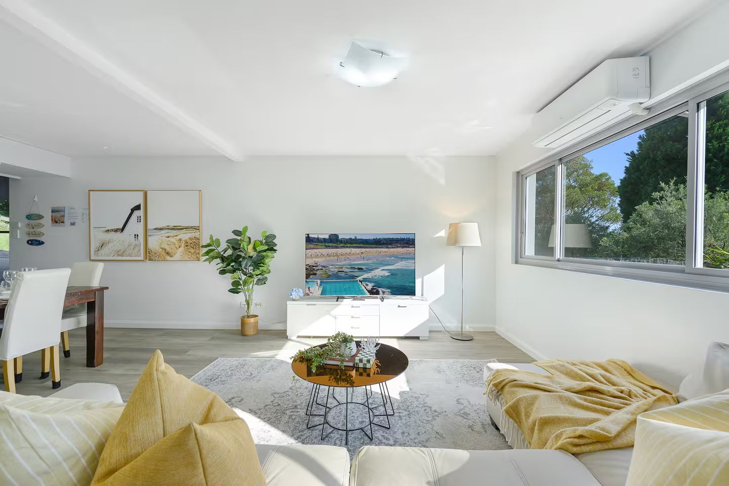 Una sala de estar moderna con un televisor grande, un comedor y vistas a una playa desde la ventana.