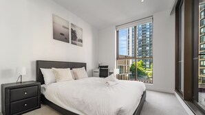Ein modernes Schlafzimmer mit einem großen Bett, einem Nachttisch, einem Beistelltisch und einem Fenster mit Blick auf die Stadt.