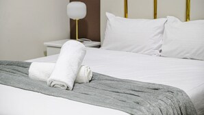 A neatly made bed with white linens and a grey throw blanket, a bedside table with a lamp, and a headboard with gold trim. - Sydney CBD 1Br with Pool/Spa/Fireworks (Pyrmont)