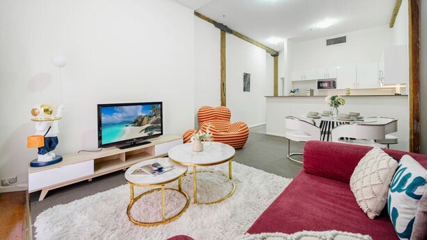 A modern living room with a TV, a sofa, a coffee table, and a striped chair. - Sydney CBD 1Br with Pool/Spa/Fireworks (Pyrmont)