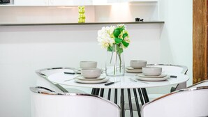 A modern dining area with a round glass table, white chairs, and a vase with flowers. - Sydney CBD 1Br with Pool/Spa/Fireworks (Pyrmont)