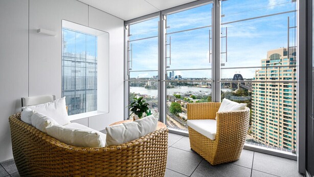 A modern living room with large windows, wicker furniture, and a view of a cityscape. - Waterfront CBD luxury 3Br best view & 2 Parkings (Barangaroo)