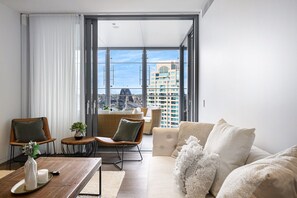 A modern living room with a sofa, chairs, a coffee table, and a view of a cityscape through large windows. - Waterfront CBD luxury 3Br best view & 2 Parkings (Barangaroo)