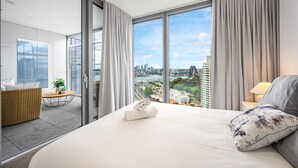 A modern hotel room with a large bed, a balcony with a city view, and a dining area with a table and chairs. - Waterfront CBD luxury 3Br best view & 2 Parkings (Barangaroo)