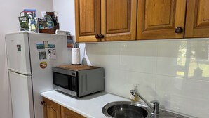 Een kleine keuken met een magnetron, een spoelbak, houten kastjes en een koelkast.