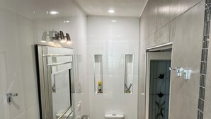 Een moderne badkamer met een glazen douchecabine, een wit toilet en een wastafel met een spiegel erboven.