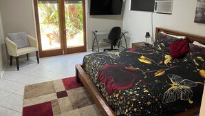 Een slaapkamer met een bed, een bureau, een stoel, een televisie en een schuifdeur naar een tuin.