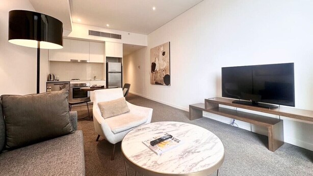 A modern living room with a sofa, a coffee table, a TV, and a kitchen in the background. - Chatswood walk to Train Station/Shopping center (Chatswood)