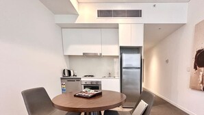 A compact kitchen with white cabinets, a stainless steel refrigerator, and a dining area with a round table and two chairs. - Chatswood walk to Train Station/Shopping center (Chatswood)