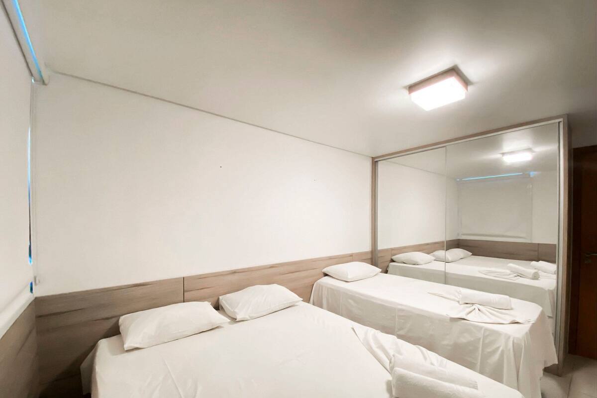 A hotel room with three single beds, a large mirror, and a ceiling light.