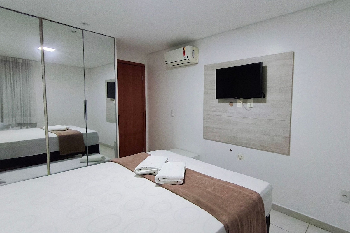 Habitación de hotel con cama, televisor de pantalla plana en la pared, espejo y unidad de aire acondicionado.