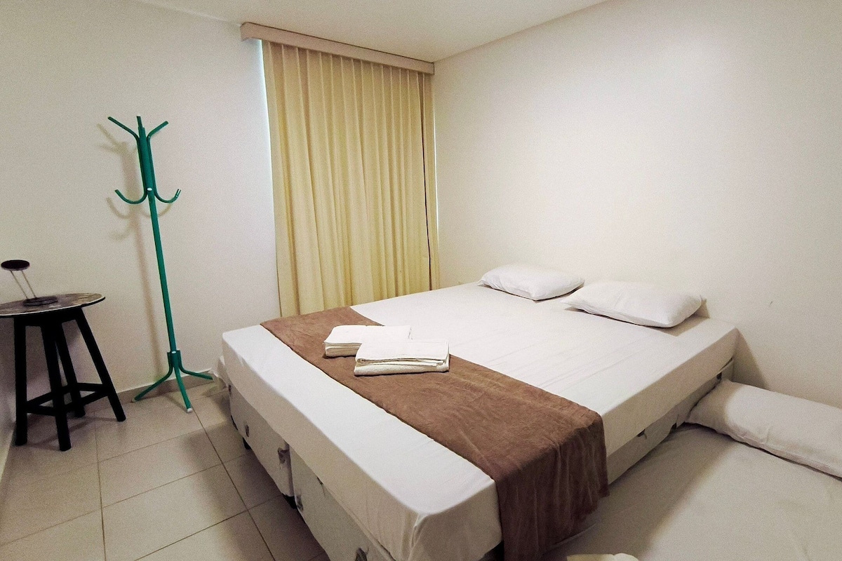 Una cama individual con cabecera marrón, ropa de cama blanca y una mesita de noche con silla.