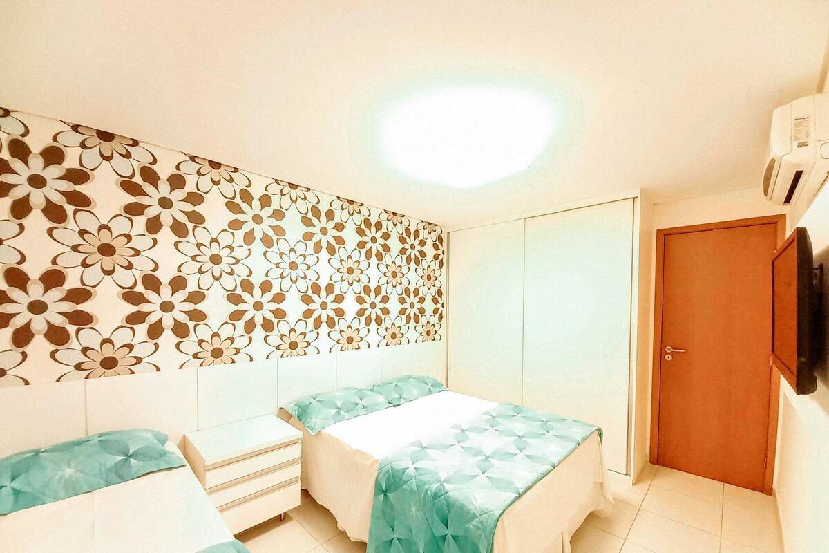 A bedroom with two beds, a wardrobe, a television, and a patterned wall.
