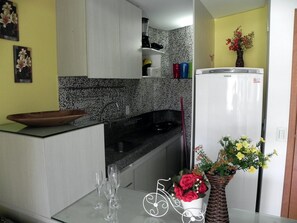 A kitchen with a black and white tiled backsplash, a white refrigerator, and a vase with flowers on the counter. - Carneiros Beach Resort by CTA (Tamandaré)