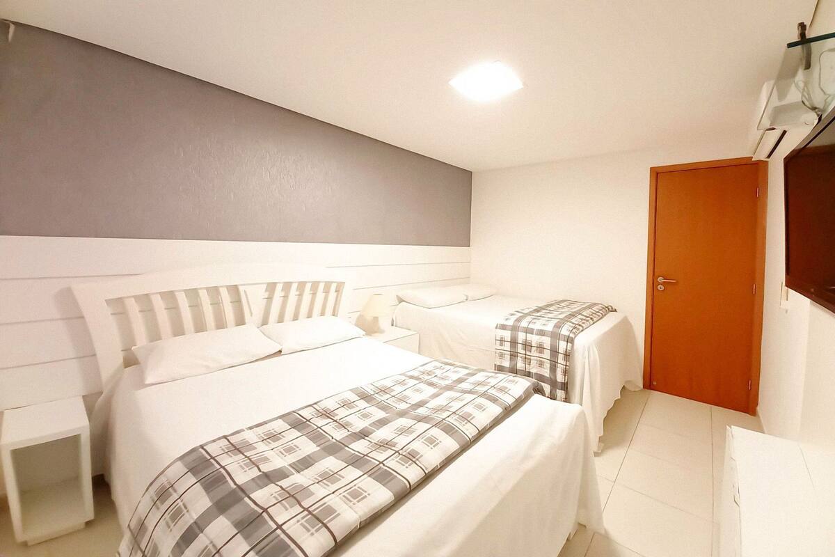 A bedroom with two beds, a wooden door, and a white nightstand.