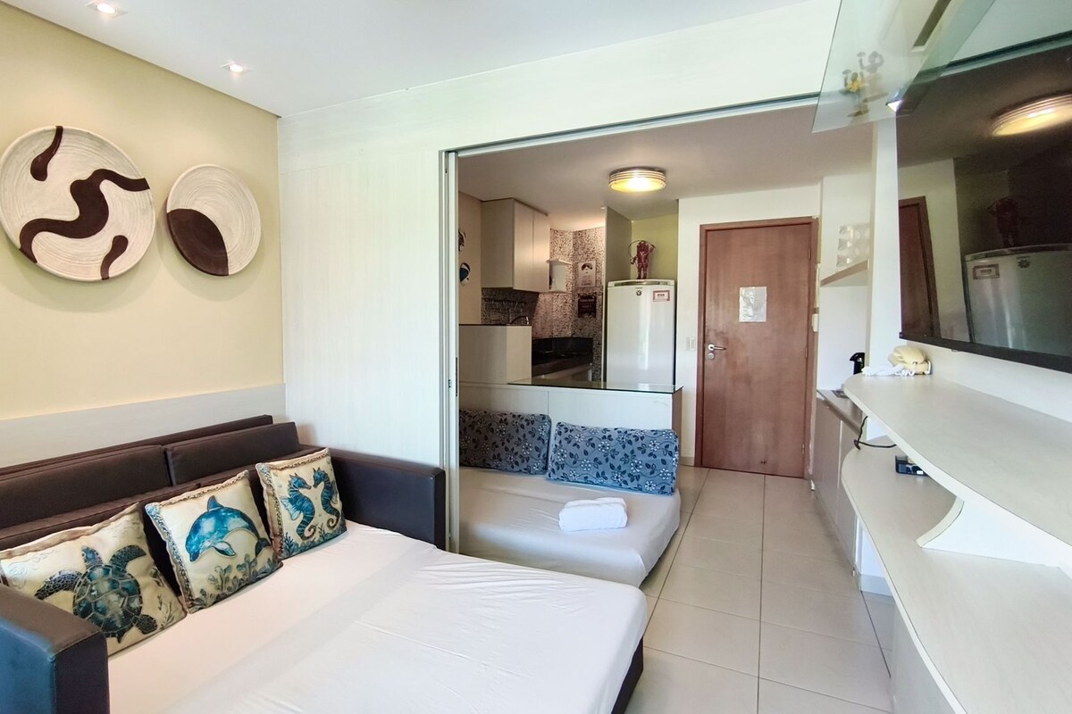 Camera d'albergo con un letto, un divano, un angolo cottura e un bagno visibile attraverso una porta aperta.