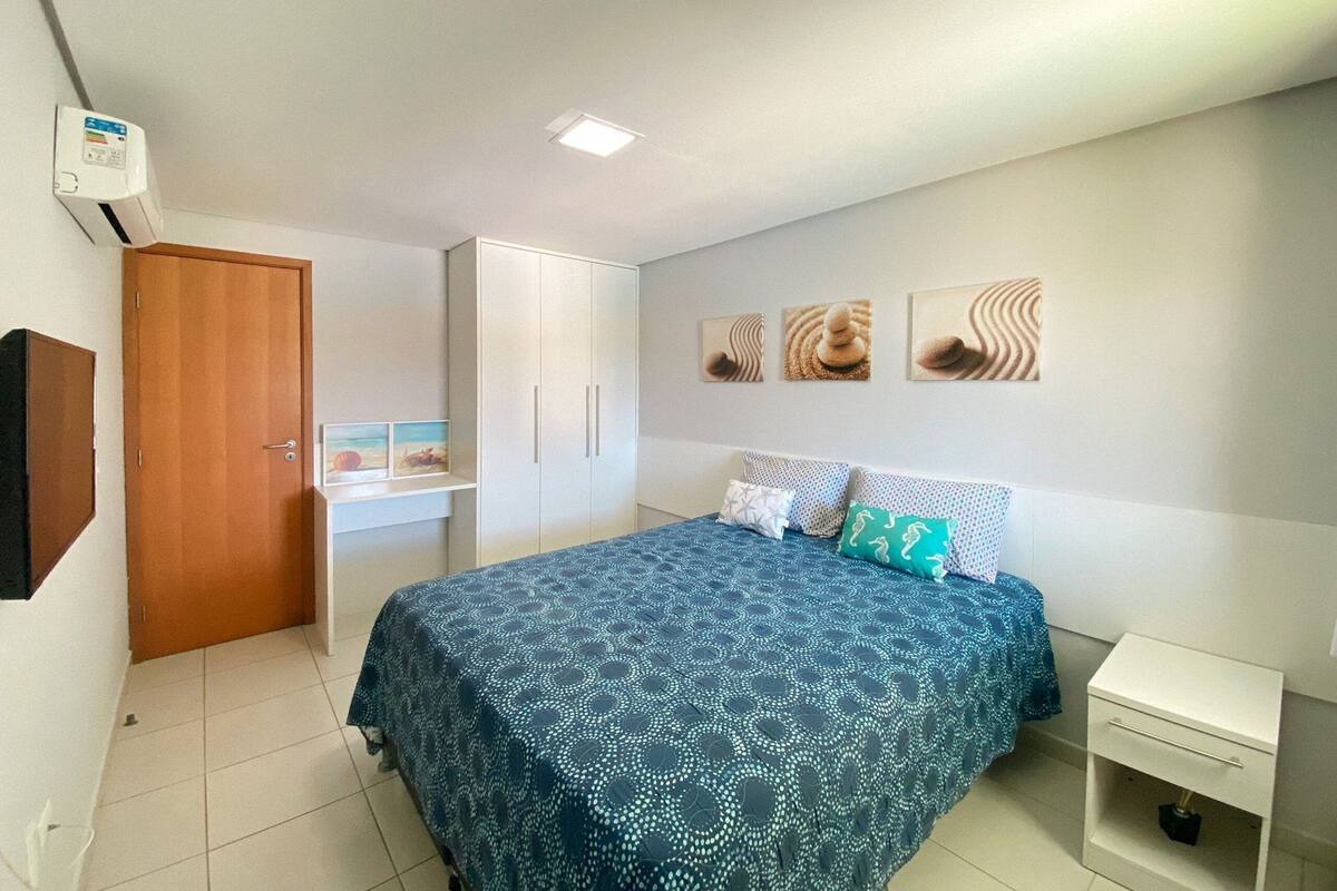 A bedroom with a bed, a wardrobe, a bedside table, and a wall-mounted air conditioner.