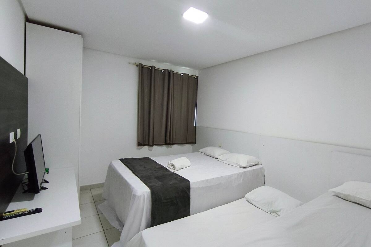 A hotel room with two single beds, a desk with a chair, a television, and a window with curtains.