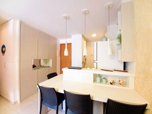 Una cocina moderna con una isla blanca, sillas negras, luces colgantes y una puerta de madera.