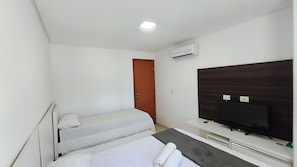 A hotel room with two single beds, a television, an air conditioning unit, and a door. - Carneiros Beach Resort by CTA (Tamandaré)