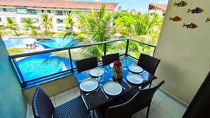 A balcony with a table set for dining, overlooking a swimming pool and lush greenery. - Carneiros Beach Resort by CTA (Tamandaré)