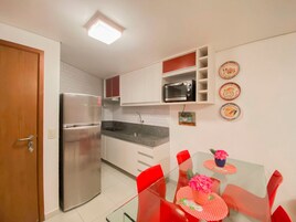 Cocina compacta con refrigerador, microondas y comedor con mesa de vidrio y sillas rojas.