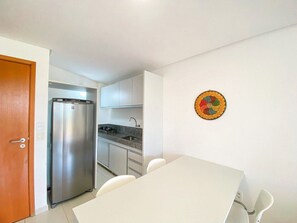 A compact kitchen with a refrigerator, a sink, and a dining table with chairs. - Carneiros Beach Resort by CTA (Tamandaré)