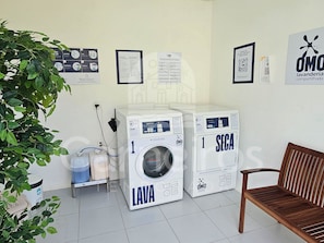A laundry area with two washing machines, a bench, and informational posters on the wall. - Carneiros Beach Resort by CTA (Tamandaré)