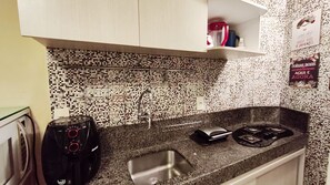 Una cocina con salpicadero de azulejos, un lavamanos de acero inoxidable, una estufa eléctrica negra y una cafetera en la encimera.